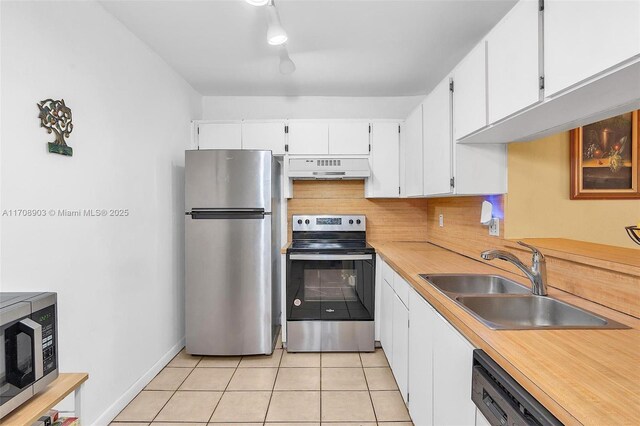 kitchen with sink, stainless steel appliances, light tile patterned floors, ventilation hood, and white cabinets