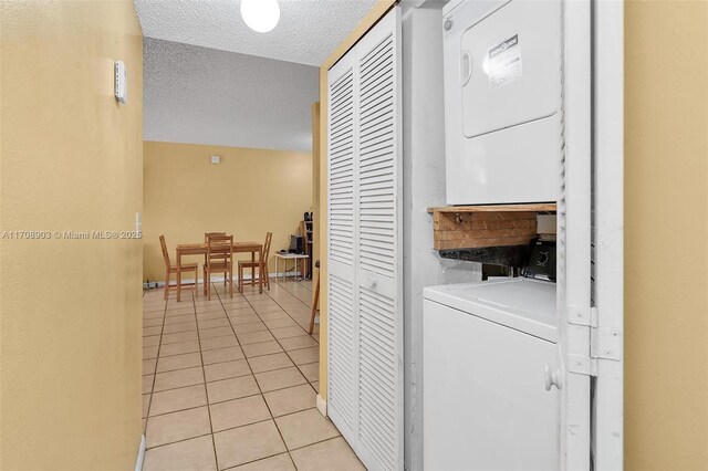 laundry area with stacked washer / dryer, light tile patterned flooring, and a textured ceiling