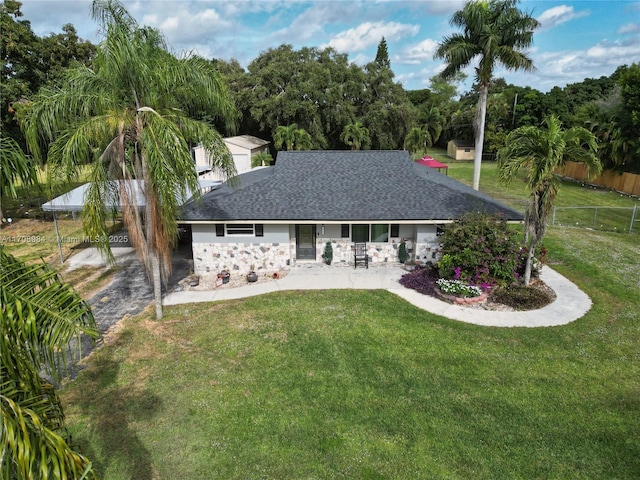 back of property with a shingled roof, fence, a lawn, a carport, and stone siding