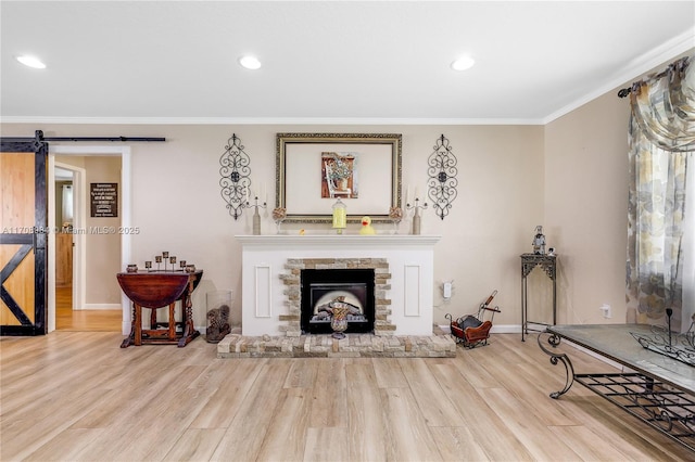 living room featuring crown molding, a fireplace, light hardwood / wood-style floors, and a barn door