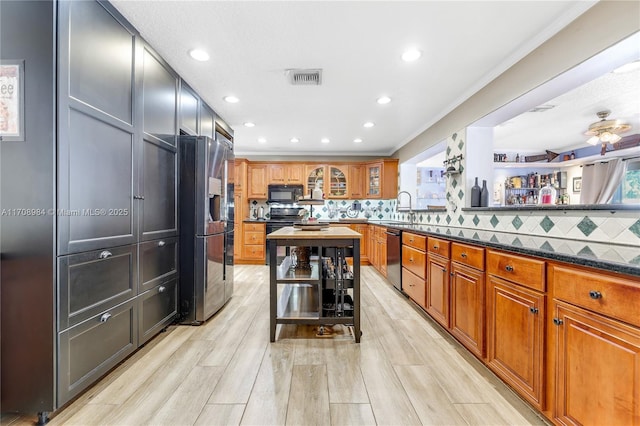 kitchen with dark stone counters, glass insert cabinets, brown cabinets, black appliances, and a sink