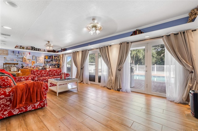 living room with visible vents, a ceiling fan, crown molding, a textured ceiling, and light wood-style floors