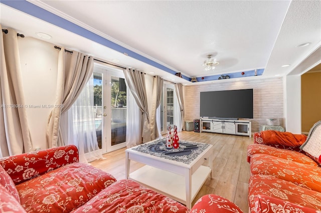 living room with light wood finished floors, a raised ceiling, ornamental molding, a textured ceiling, and french doors