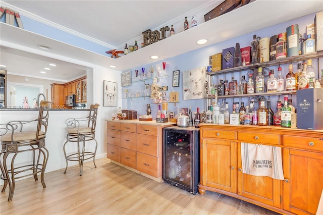 bar with crown molding, a dry bar, stainless steel microwave, light wood-type flooring, and beverage cooler