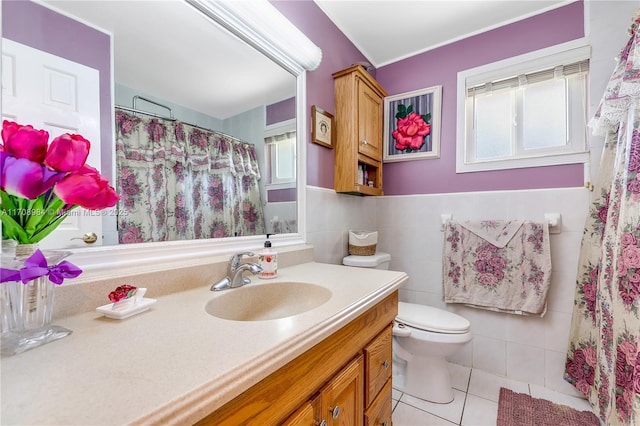 bathroom with wainscoting, toilet, tile patterned floors, vanity, and tile walls