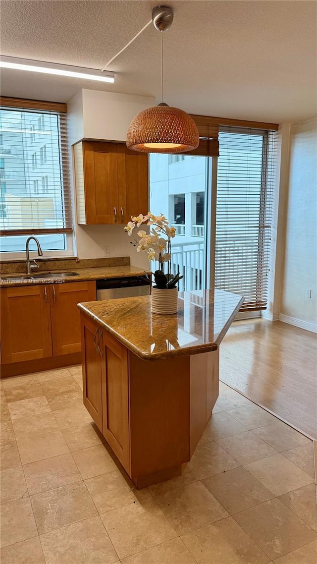 kitchen with light stone counters, stainless steel dishwasher, sink, decorative light fixtures, and a kitchen island