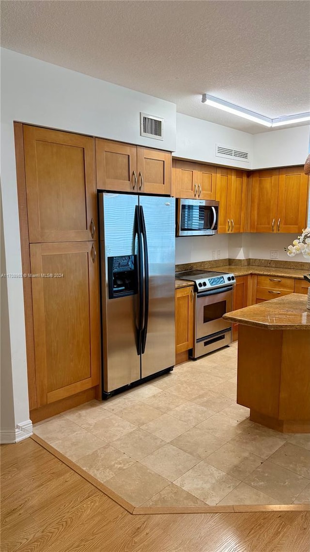 kitchen with appliances with stainless steel finishes, a textured ceiling, and light hardwood / wood-style floors