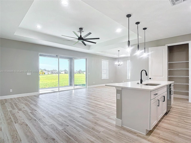 kitchen with a kitchen island with sink, hanging light fixtures, sink, light wood-type flooring, and a tray ceiling