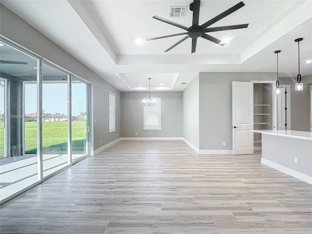 unfurnished living room featuring ceiling fan with notable chandelier, light wood-type flooring, and a tray ceiling