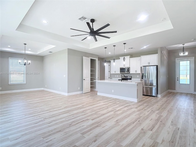 kitchen with appliances with stainless steel finishes, a tray ceiling, light hardwood / wood-style flooring, and a center island with sink