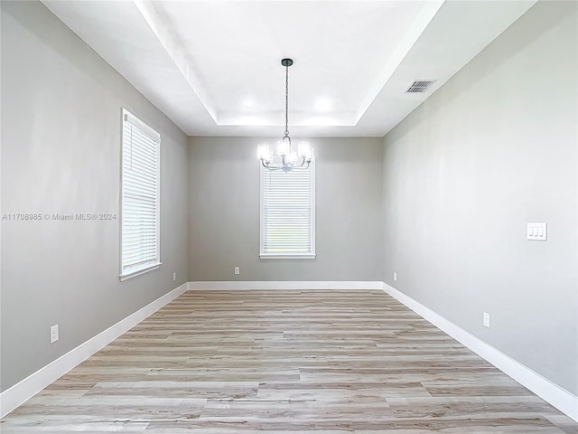 spare room featuring a raised ceiling, plenty of natural light, light hardwood / wood-style floors, and an inviting chandelier