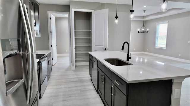 kitchen featuring light stone countertops, stainless steel appliances, a kitchen island with sink, sink, and hanging light fixtures