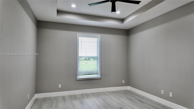 empty room featuring light wood-type flooring, a tray ceiling, and ceiling fan