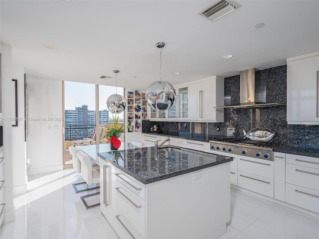 kitchen featuring backsplash, wall chimney exhaust hood, stainless steel gas cooktop, white cabinetry, and hanging light fixtures