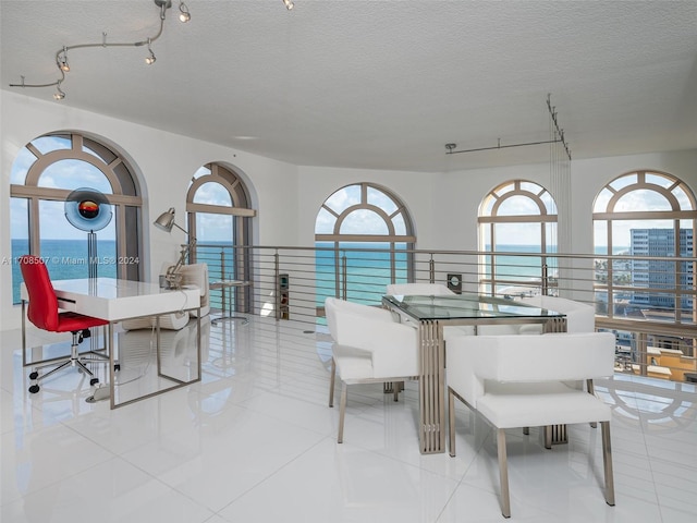 tiled dining area with a textured ceiling, a water view, and track lighting