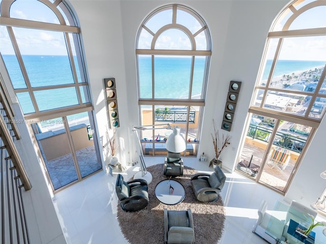 tiled living room featuring a towering ceiling, plenty of natural light, and a water view