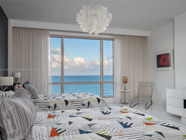 bedroom with a textured ceiling, a water view, and a notable chandelier