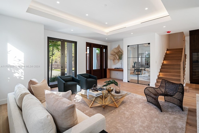 living room featuring a raised ceiling, light hardwood / wood-style flooring, and french doors