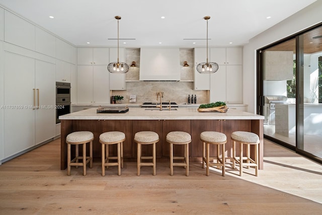 kitchen with pendant lighting, white cabinetry, premium range hood, and a large island with sink