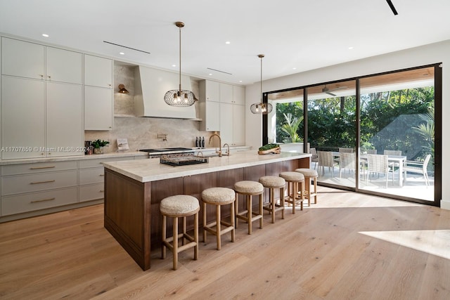 kitchen featuring white cabinetry, light hardwood / wood-style flooring, hanging light fixtures, and an island with sink