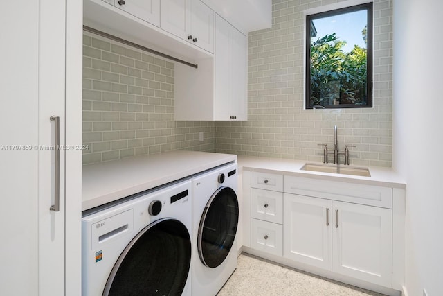 clothes washing area with washing machine and clothes dryer, sink, and cabinets