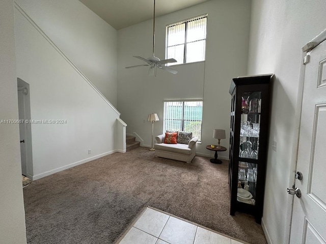 living room featuring ceiling fan, a healthy amount of sunlight, light colored carpet, and a towering ceiling