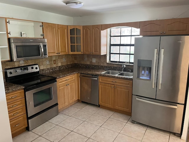 kitchen with decorative backsplash, appliances with stainless steel finishes, dark stone counters, sink, and light tile patterned floors