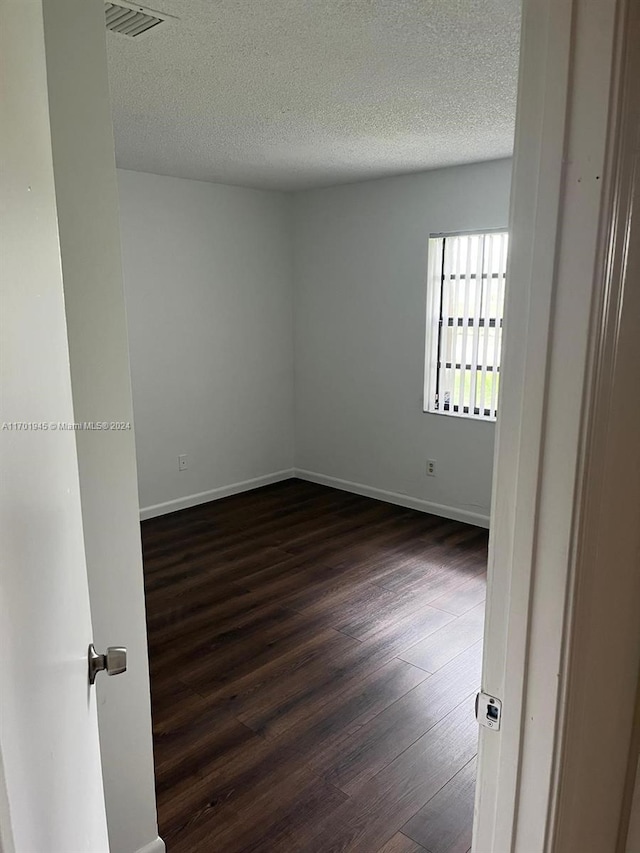 empty room with a textured ceiling and dark hardwood / wood-style floors