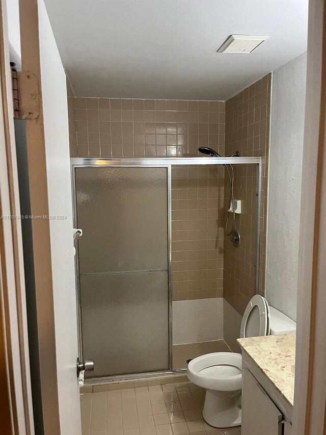 bathroom featuring tile patterned flooring, vanity, a shower with door, and toilet