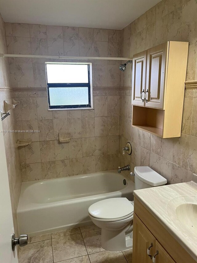 full bathroom with vanity, tile patterned floors, tiled shower / bath, toilet, and tile walls