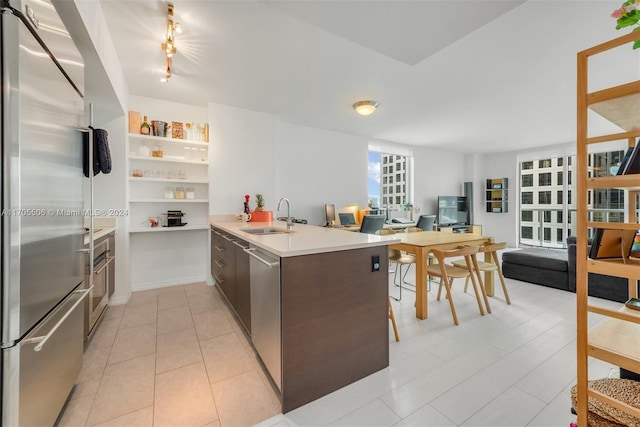 kitchen featuring dark brown cabinetry, sink, kitchen peninsula, light tile patterned floors, and appliances with stainless steel finishes