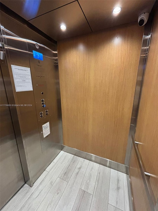 room details with hardwood / wood-style floors, wood walls, and elevator