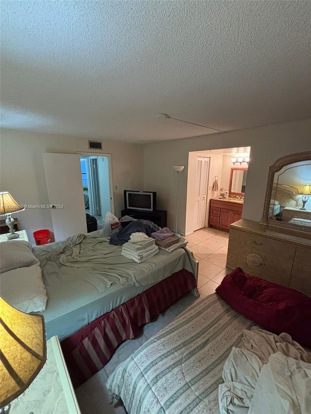 bedroom featuring light tile patterned floors, a textured ceiling, and connected bathroom