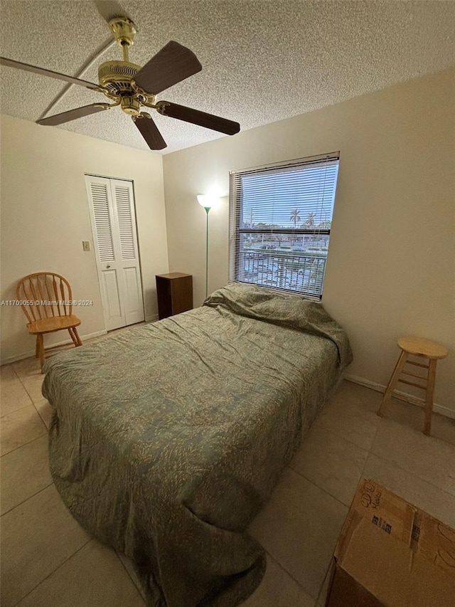 bedroom with ceiling fan, a closet, light tile patterned floors, and a textured ceiling