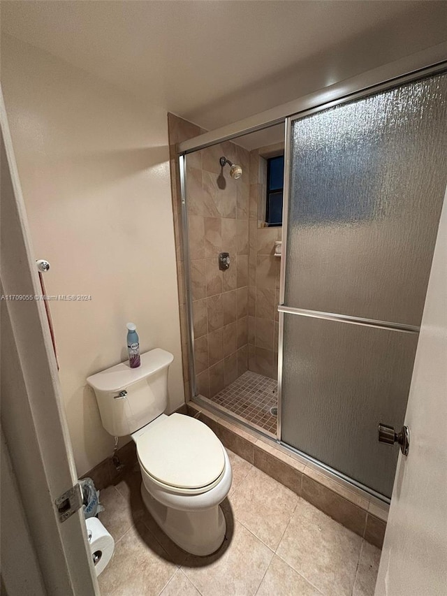 bathroom with tile patterned flooring, toilet, and a shower with door