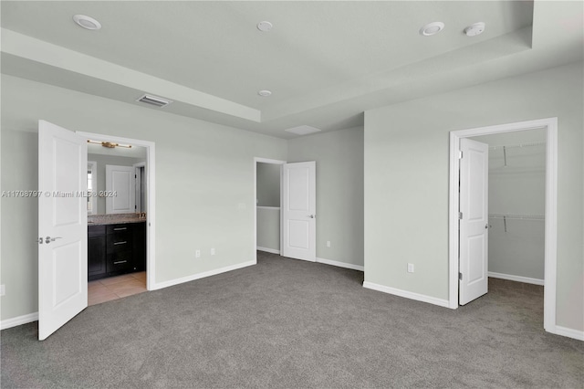 unfurnished bedroom with ensuite bathroom, light colored carpet, a spacious closet, and a tray ceiling