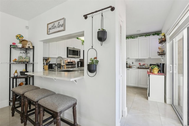 kitchen with white cabinets, sink, a breakfast bar area, kitchen peninsula, and stainless steel appliances