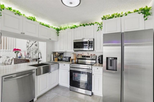 kitchen featuring sink, stainless steel appliances, white cabinets, a textured ceiling, and light tile patterned flooring