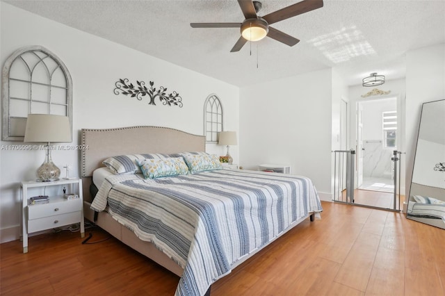 bedroom with ceiling fan, wood-type flooring, a textured ceiling, and ensuite bath