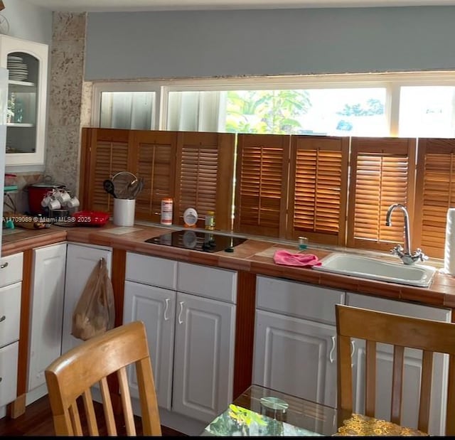 kitchen featuring black electric stovetop, tile counters, white cabinetry, and sink