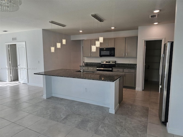 kitchen with stainless steel appliances, sink, a center island with sink, dark stone countertops, and hanging light fixtures