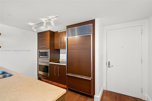 kitchen with built in appliances, dark hardwood / wood-style flooring, and sink