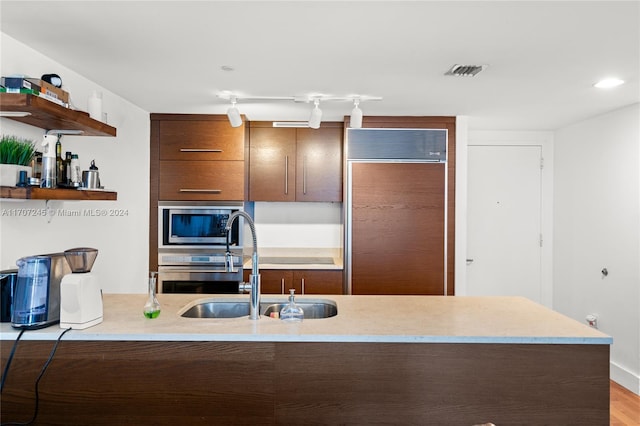 kitchen with kitchen peninsula, appliances with stainless steel finishes, light wood-type flooring, and sink