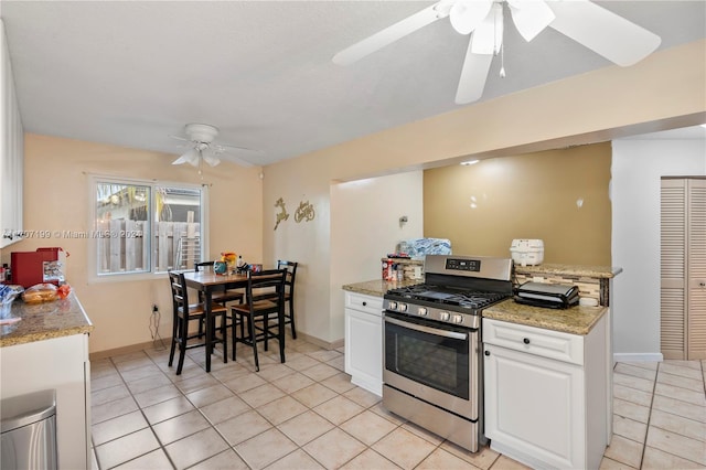 kitchen featuring light stone countertops, ceiling fan, white cabinets, stainless steel gas stove, and light tile patterned flooring