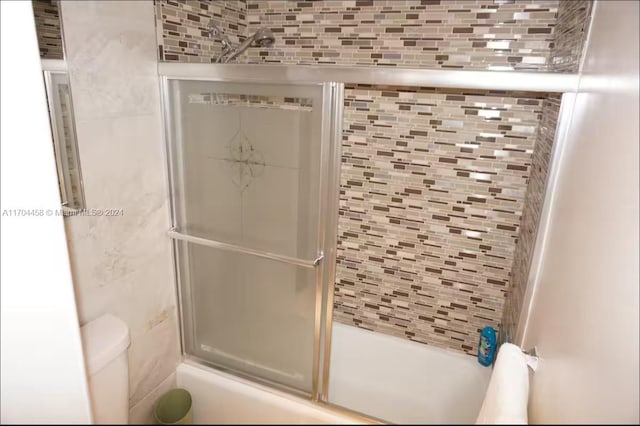 bathroom with toilet, bath / shower combo with glass door, and tasteful backsplash