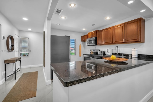 kitchen featuring sink, dark stone countertops, light tile patterned flooring, kitchen peninsula, and stainless steel appliances