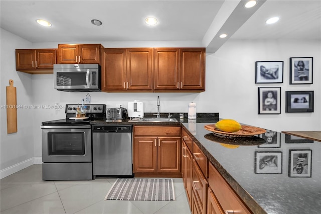 kitchen with appliances with stainless steel finishes, light tile patterned floors, dark stone countertops, and sink