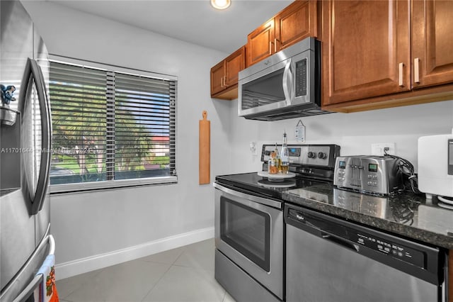 kitchen featuring appliances with stainless steel finishes, light tile patterned floors, and dark stone countertops