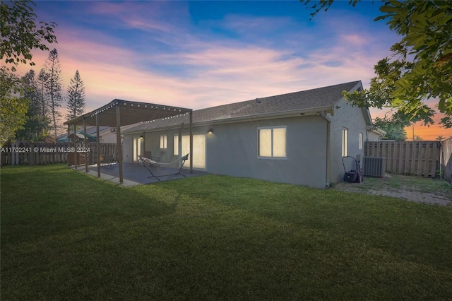 back house at dusk featuring a lawn, cooling unit, and a patio