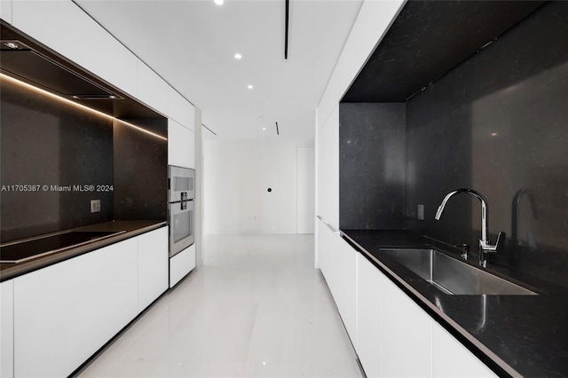 kitchen featuring black electric stovetop, white cabinets, sink, and dark stone counters